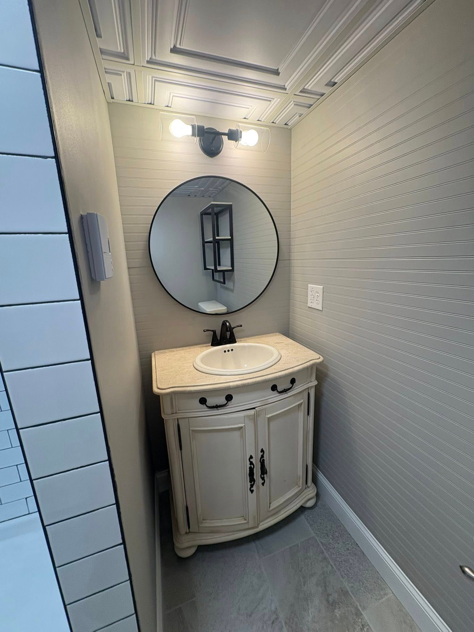 Small bathroom with a white vanity, round mirror, and textured gray walls.