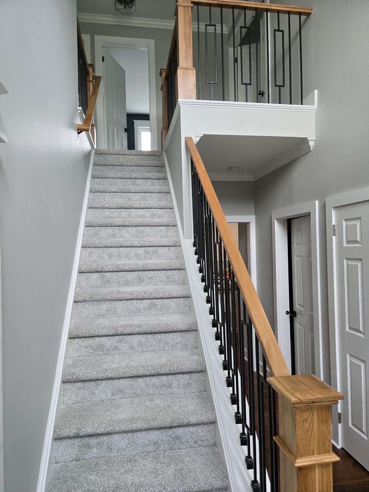 Staircase with gray carpet, wood banisters, and black metal spindles leading to upper level.