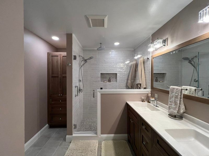 Bathroom with walk-in shower, double vanity, and tall cabinet in a remodeled space.
