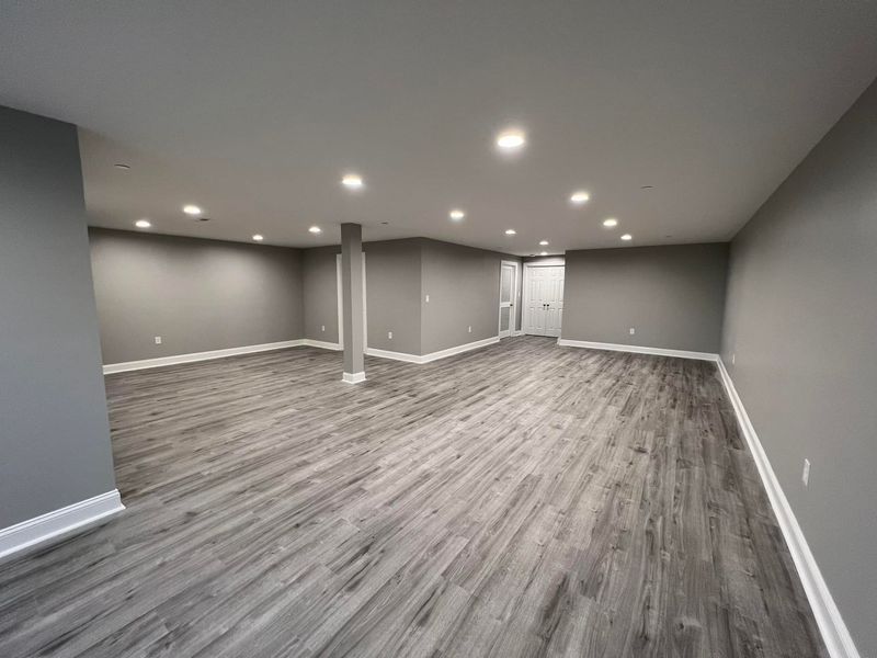 Empty, remodeled room with gray walls, wood-look flooring, recessed lighting. White trim and door.