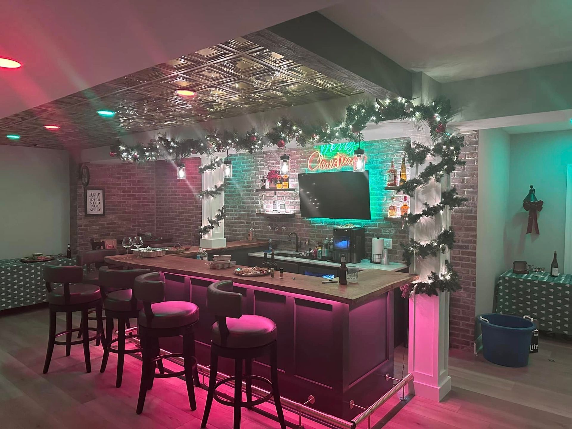A bar with red and green lighting, brick accents, and holiday decorations, including garlands.