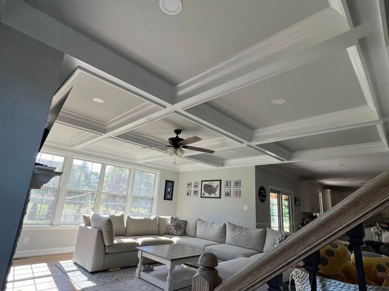 Bright living room with gray sectional sofa, coffered ceiling, ceiling fan, and large windows