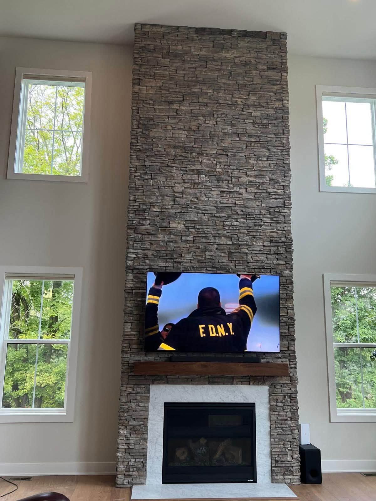 Living room with stone fireplace, TV, and tall windows in a bright, modern space
