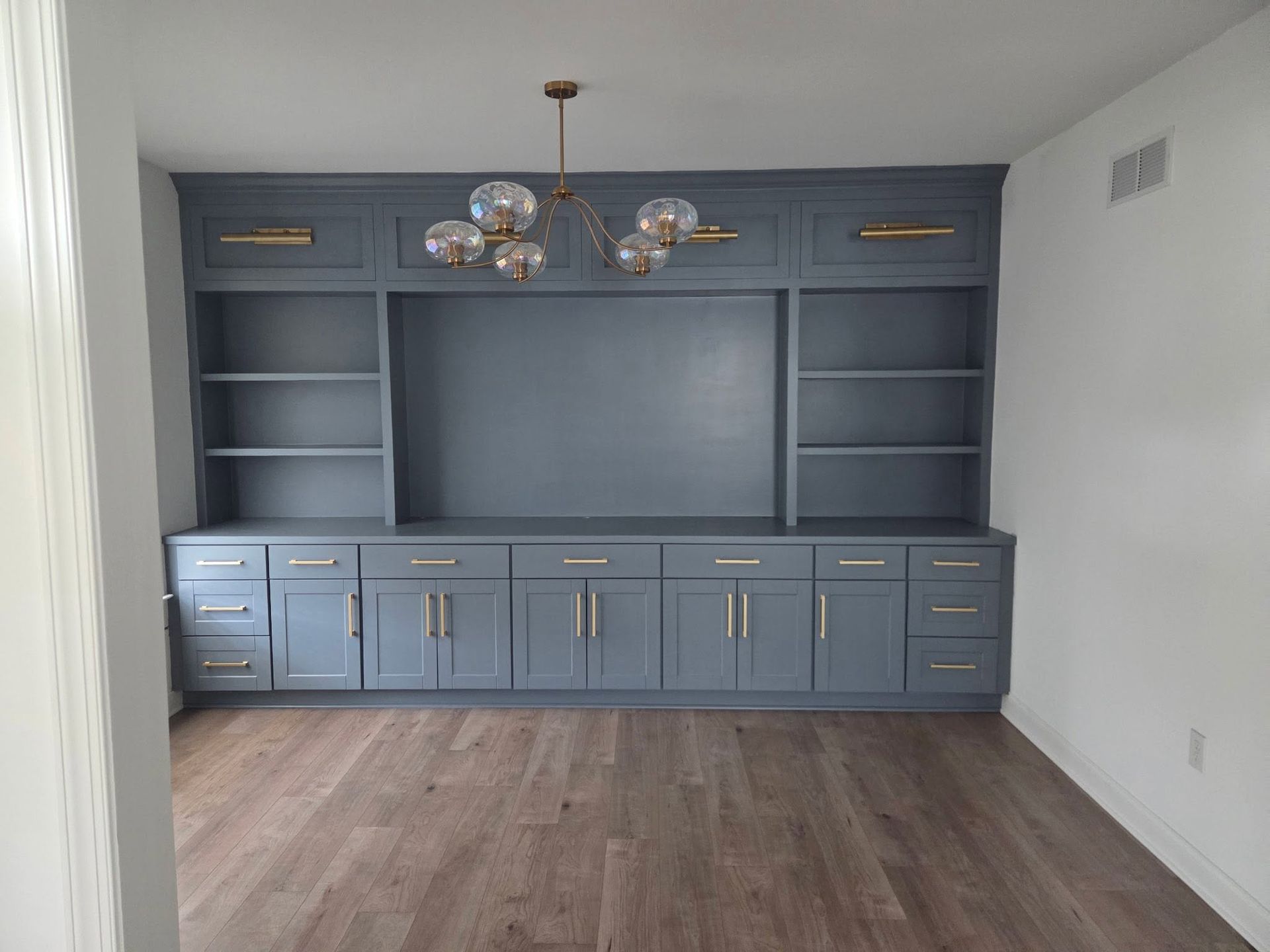 Empty living room with built-in blue cabinets, shelving, chandelier, and wood flooring