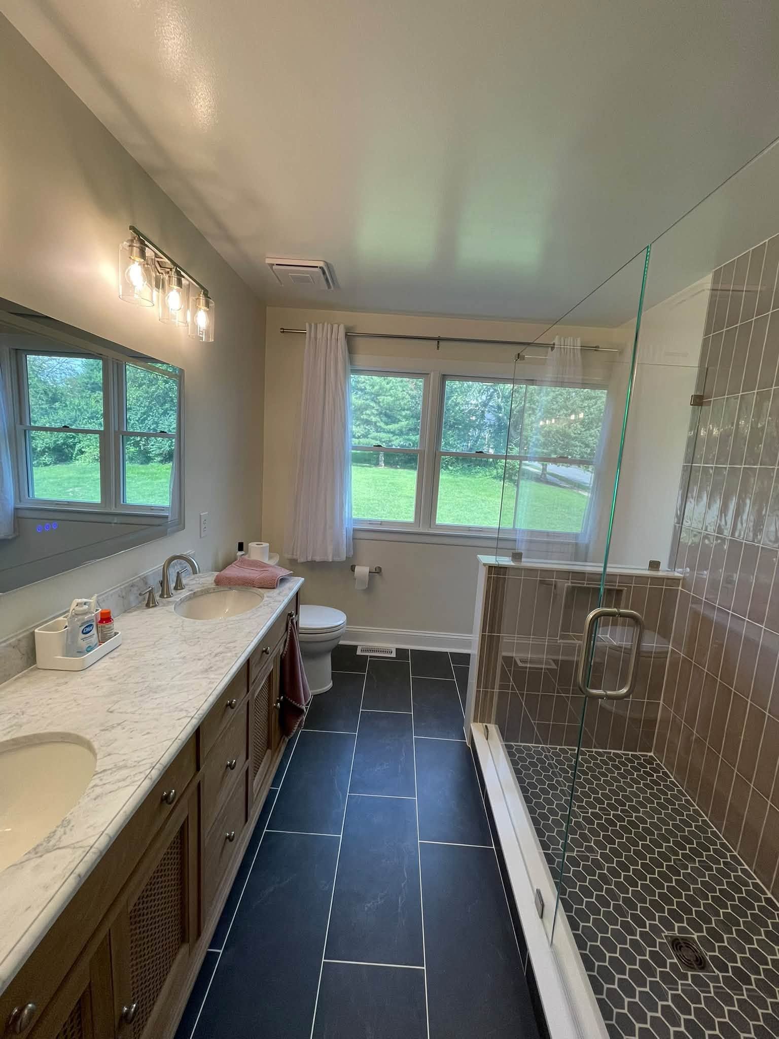 Bright bathroom with long vanity, large mirror, window, and tiled shower and tub combo.