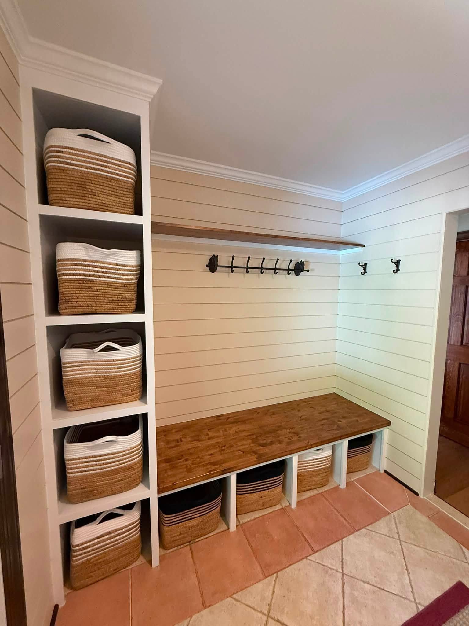 Built-in mudroom bench with cubbies, wicker baskets, hooks, and tiled floor in a bright entryway