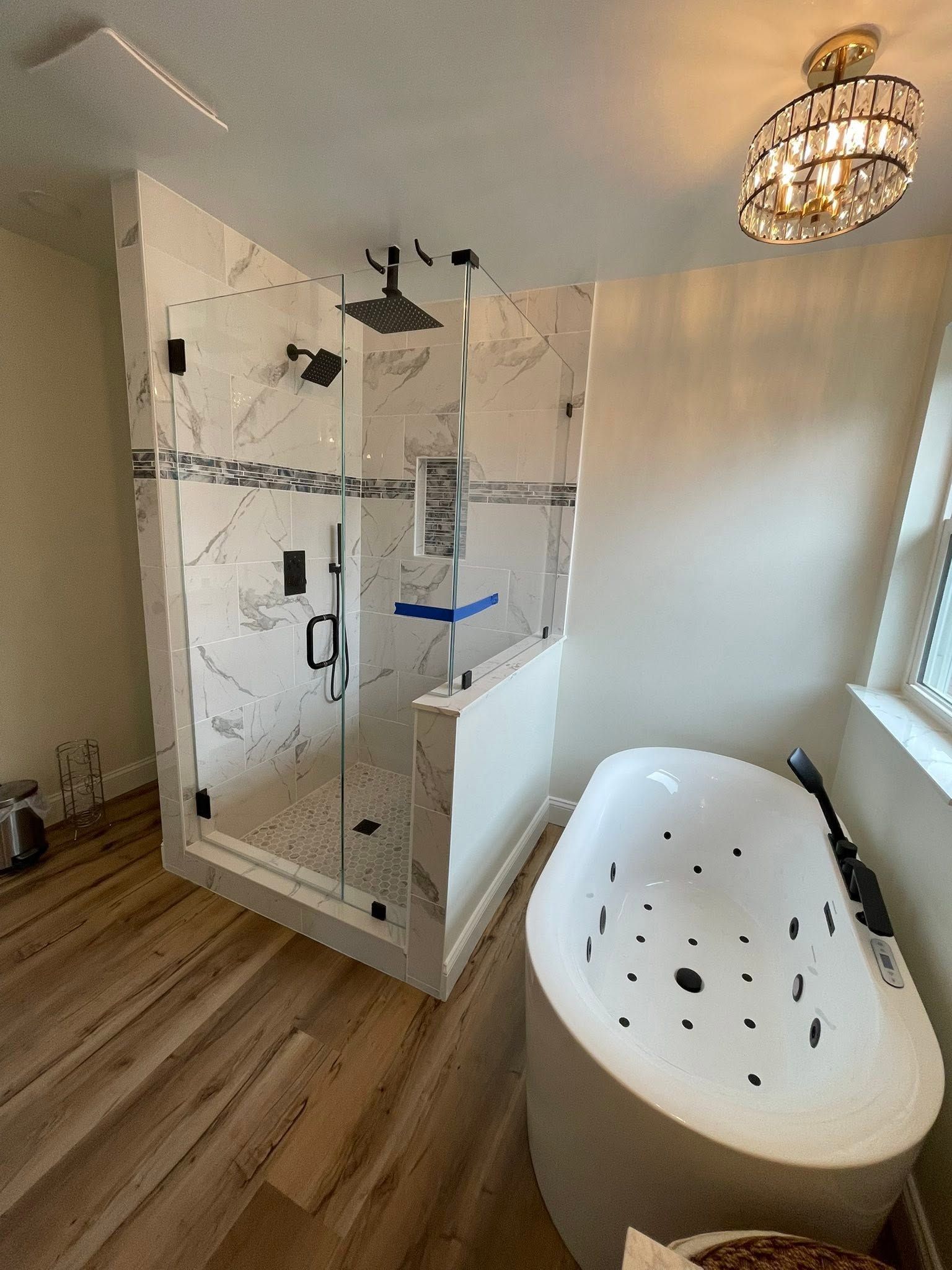 Modern bathroom with glass shower, freestanding white tub, wood floor, and chandelier lighting