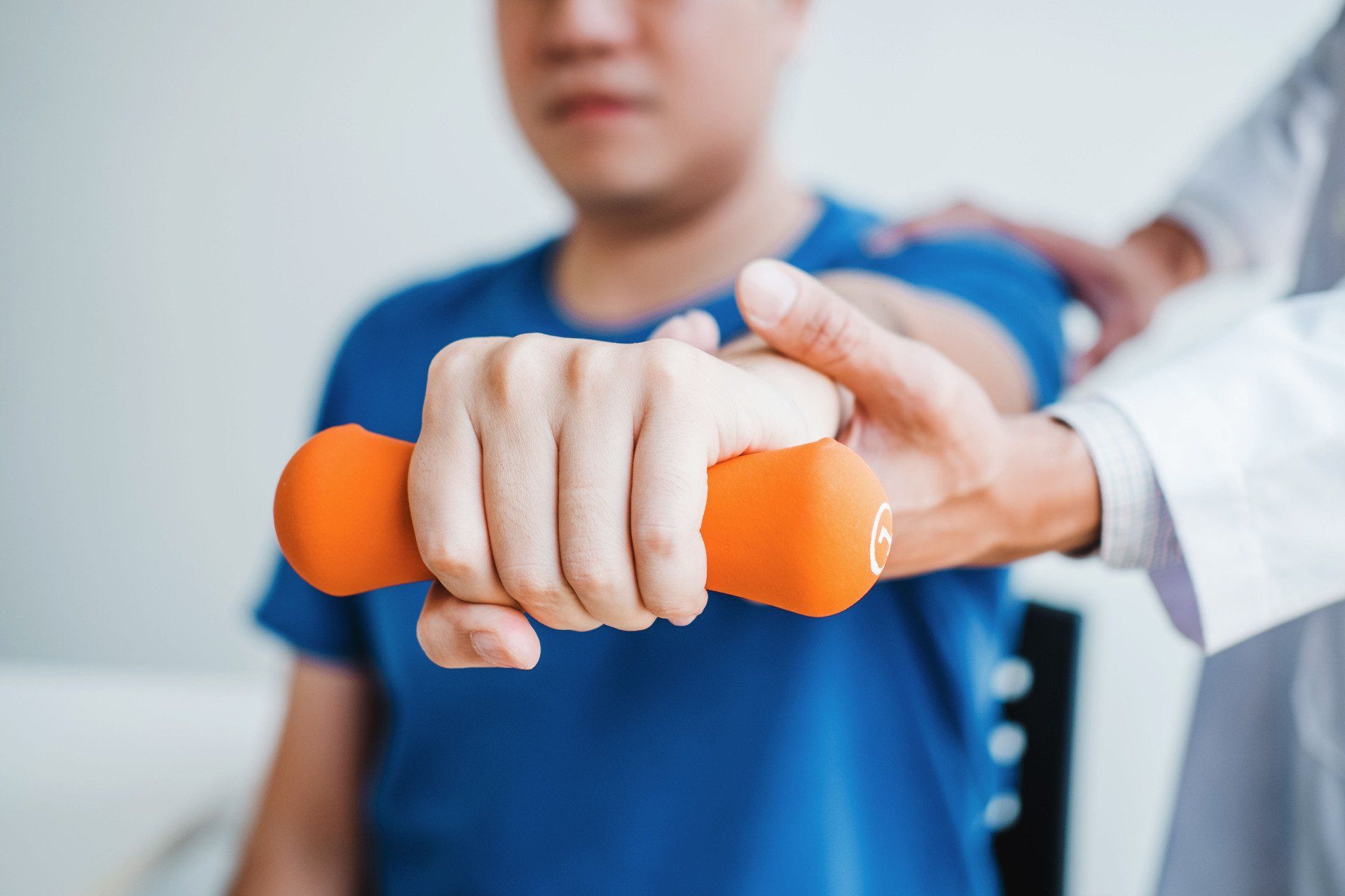 Hand holding an orange dumbbell during a physical therapy session