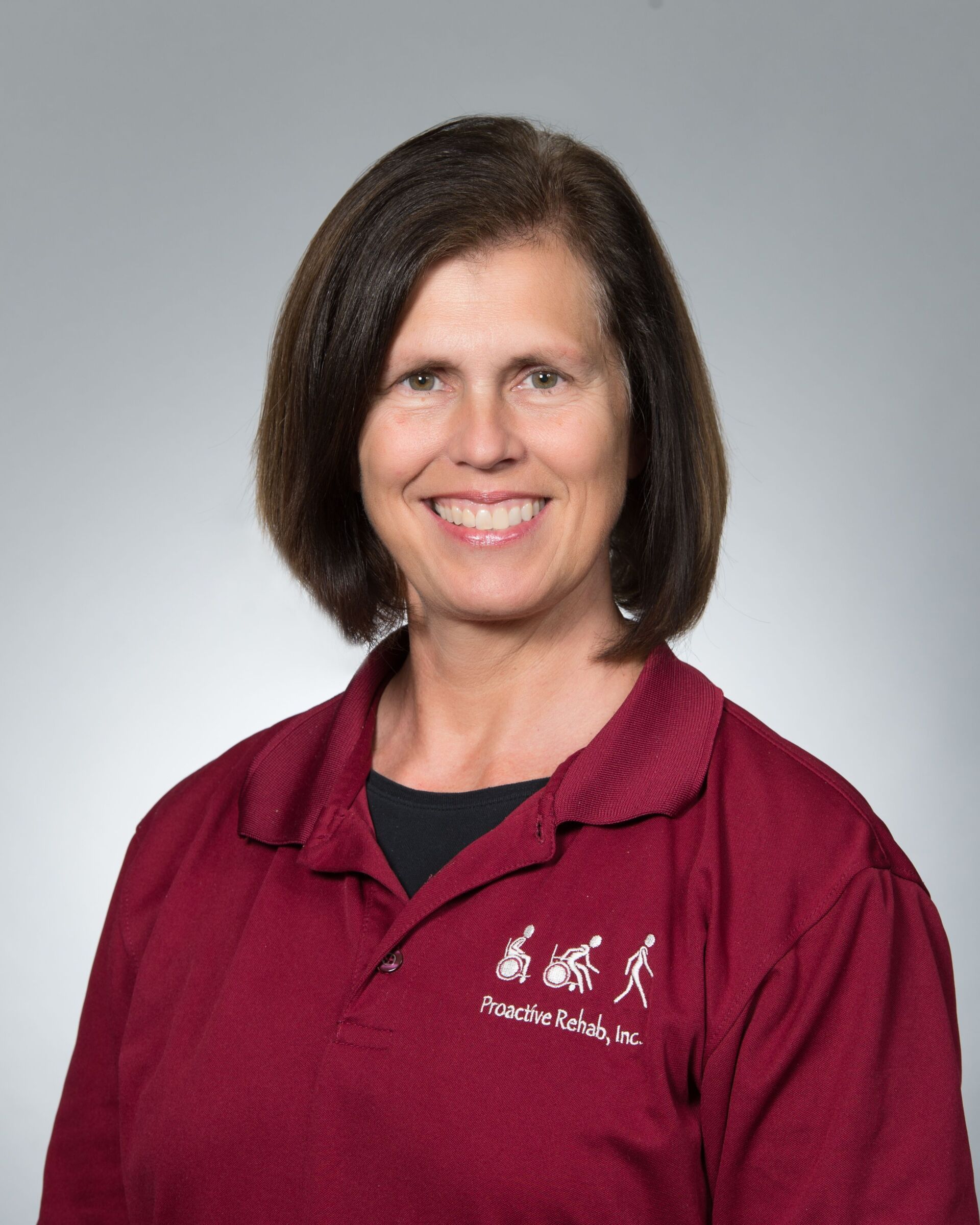 Woman in maroon polo shirt smiling against a gray background
