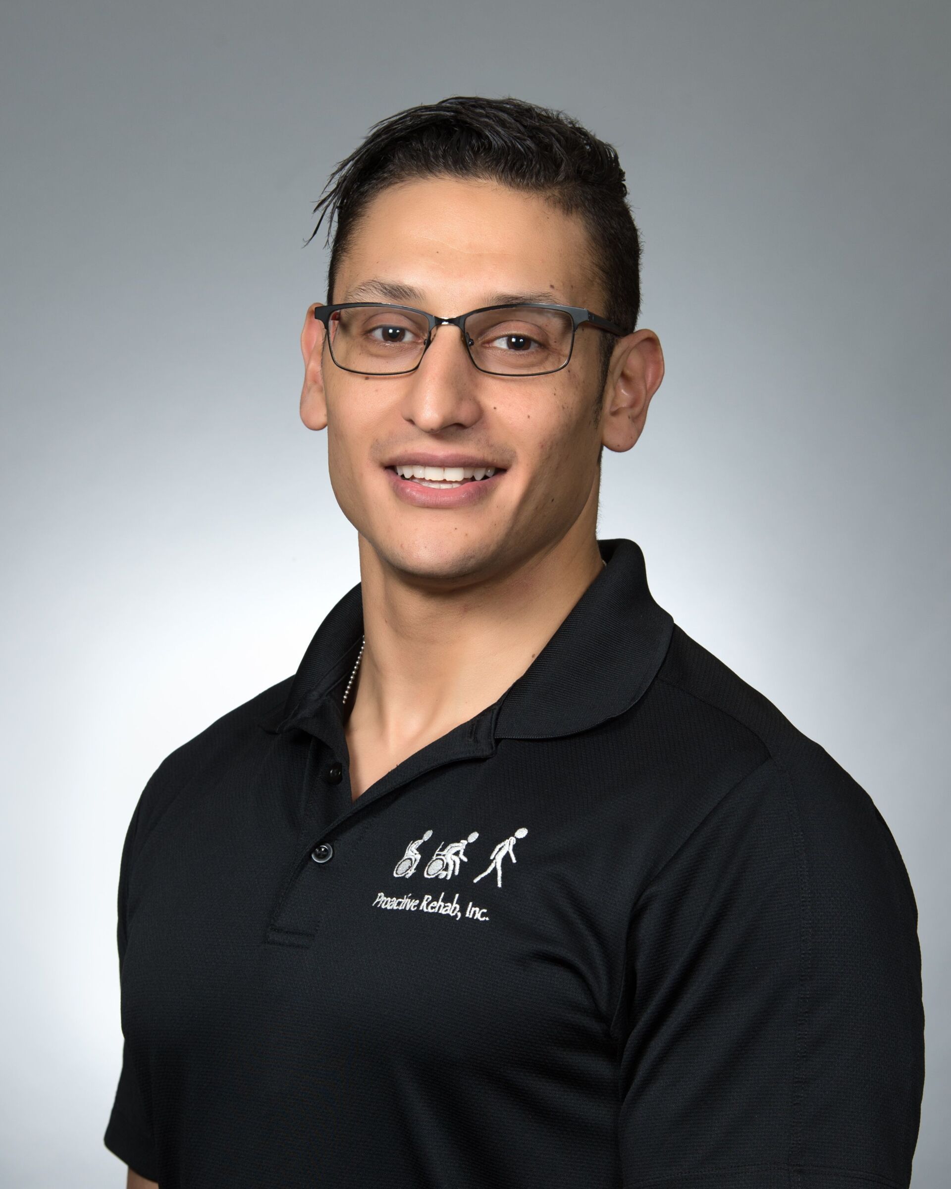 Portrait of a smiling person in glasses wearing a black collared shirt against a gray background