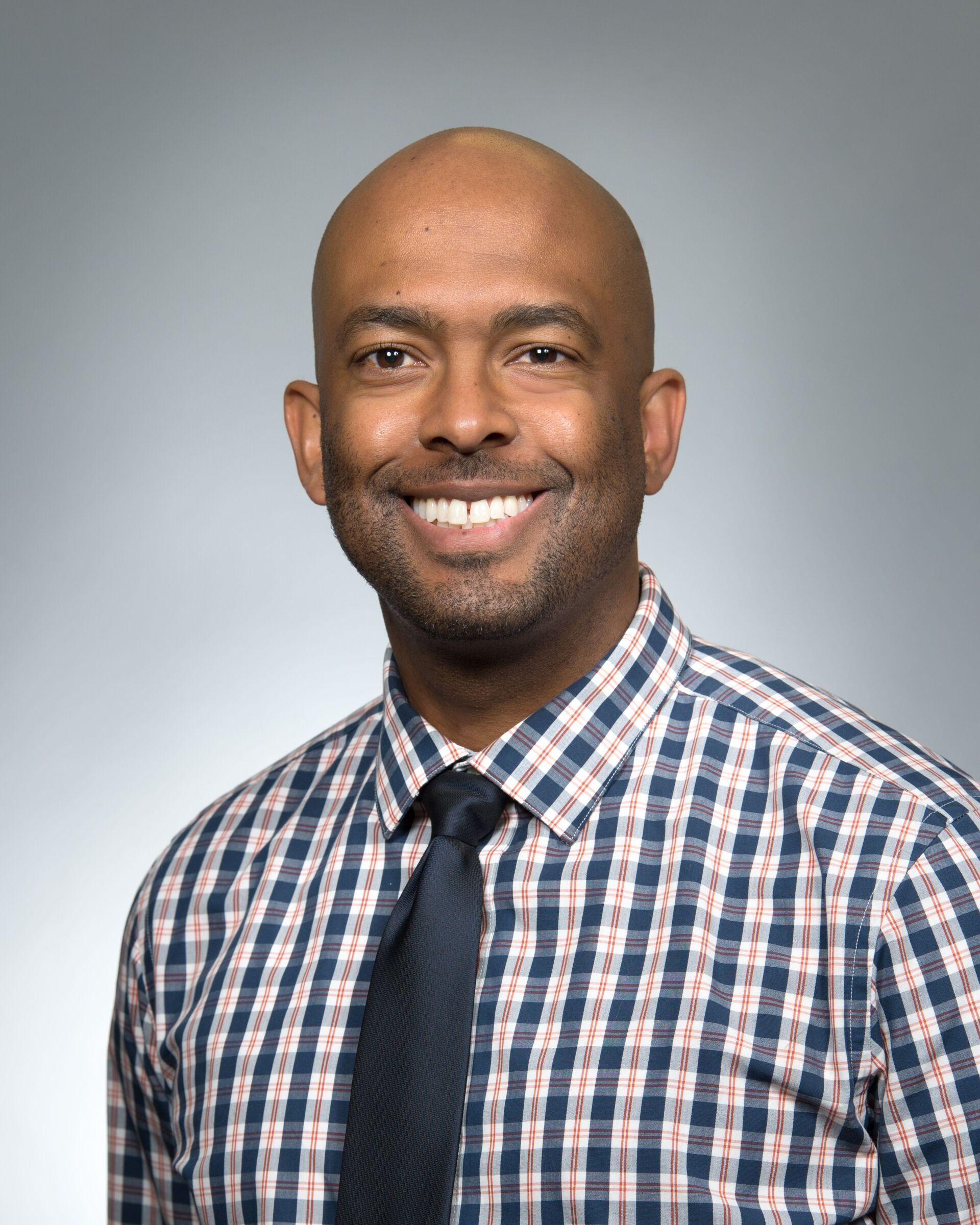 Smiling person in a checkered shirt and tie against a gray studio background