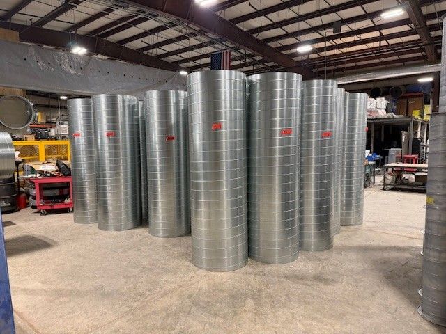 Tall, cylindrical galvanized steel ducts stand in a row on the concrete floor of a large industrial warehouse.