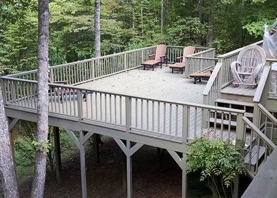 A large wooden deck with chairs and stairs in the woods.
