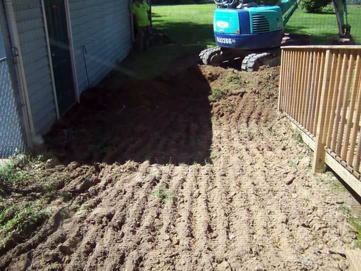 A blue excavator is digging a hole in the dirt in front of a house.