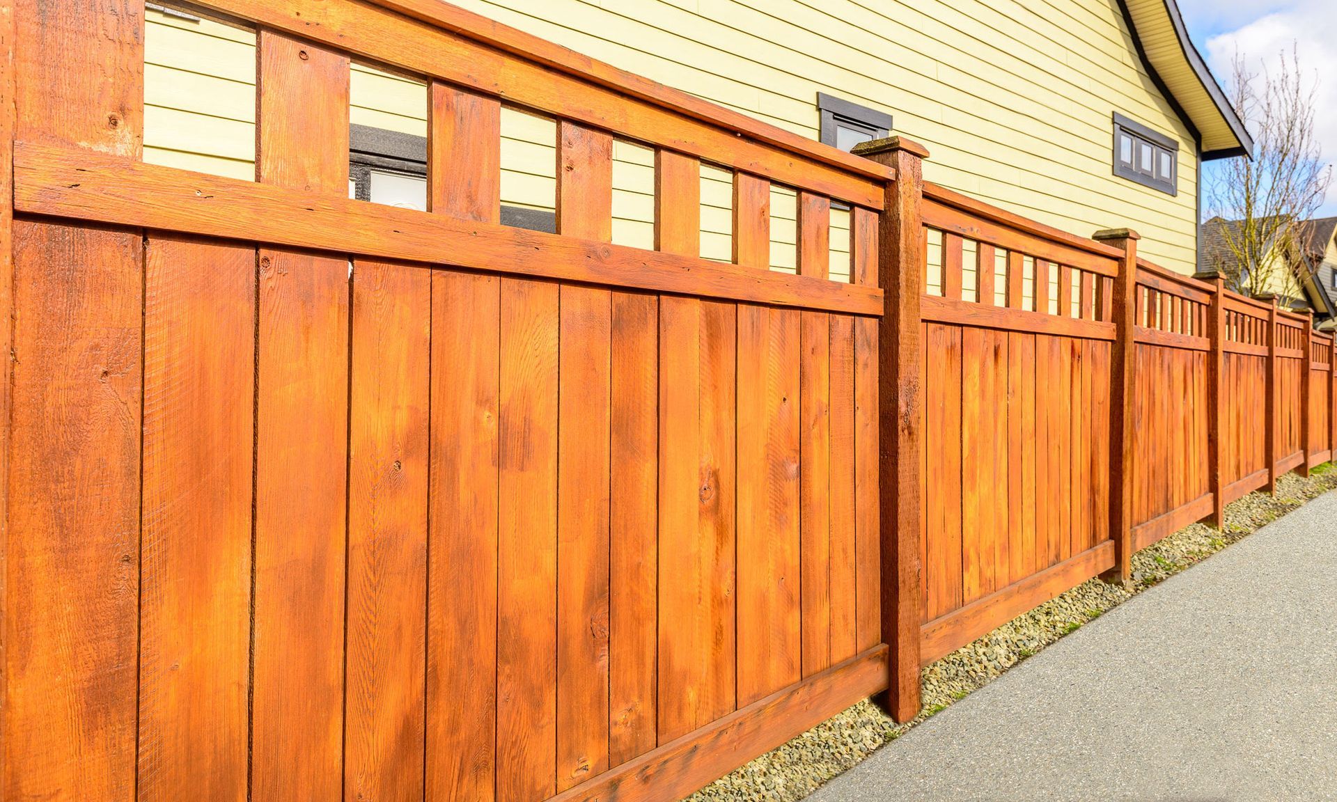 A wooden fence along a sidewalk in front of a house.