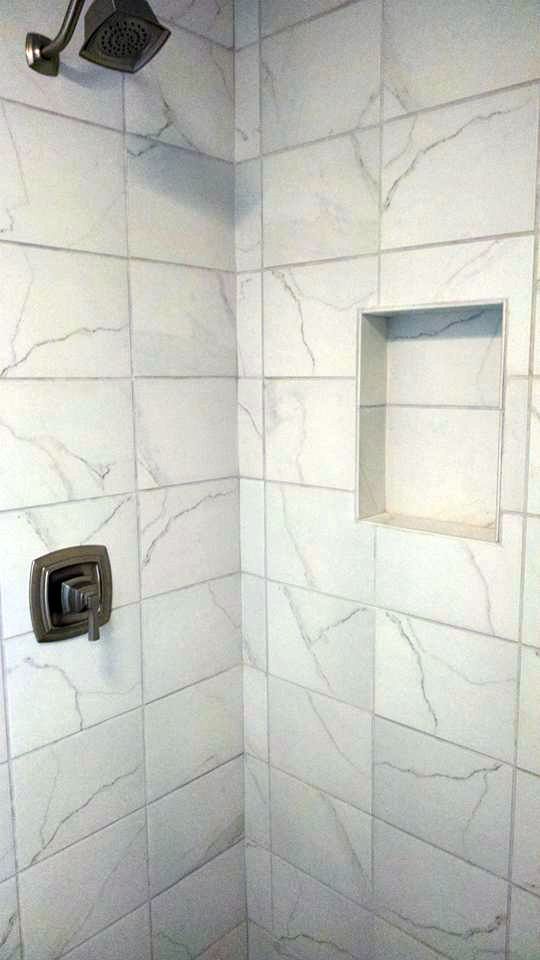 A shower with white tiles and a shelf in the corner.