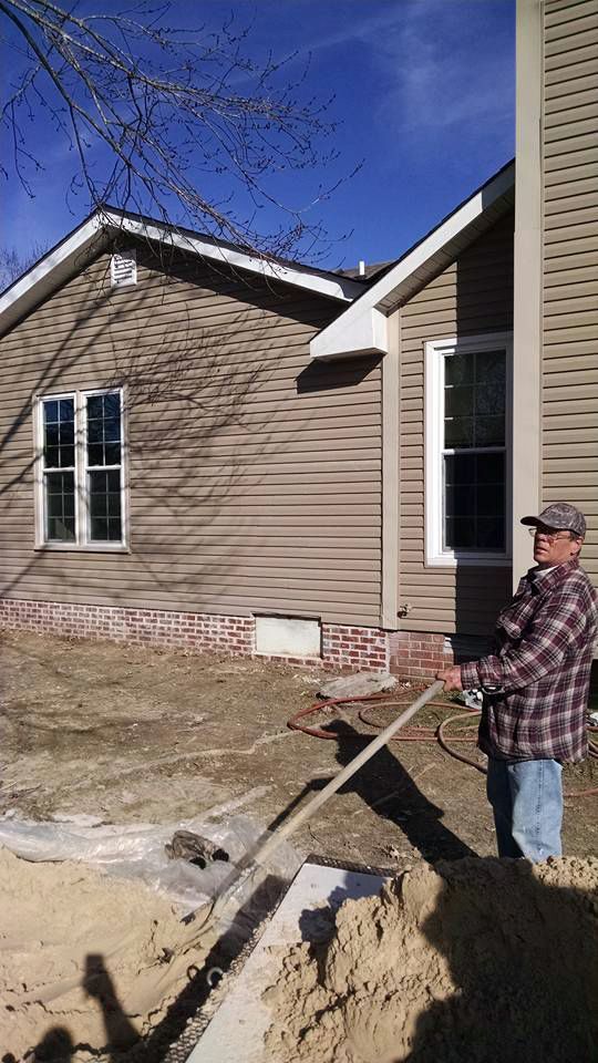 A man is standing in front of a house holding a shovel.