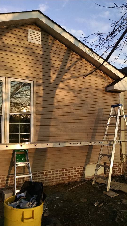 A ladder is sitting on the side of a house next to a yellow bucket.
