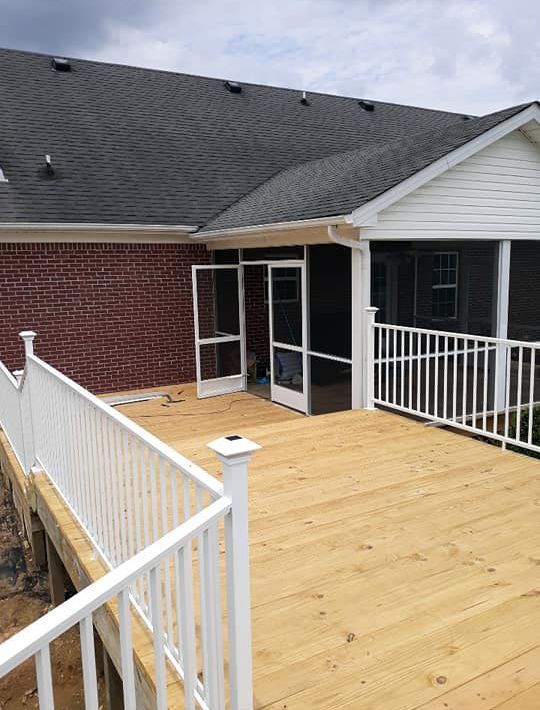 A screened in porch with a wooden deck and white railing.