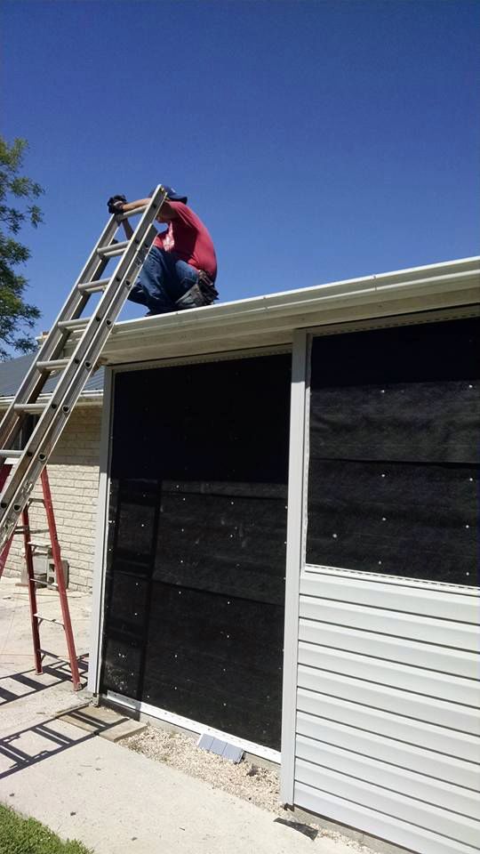 A man is sitting on a ladder on the roof of a garage.