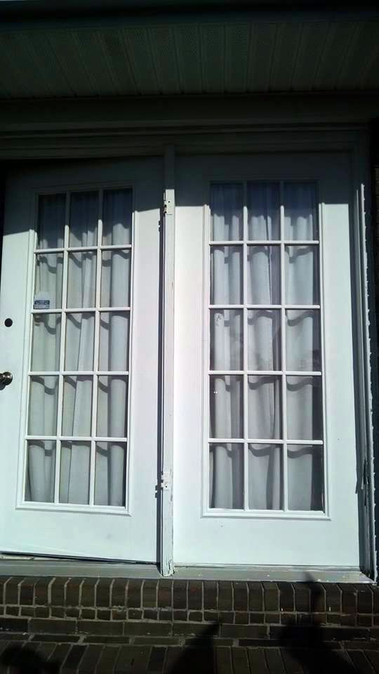 A pair of white french doors are open on a brick wall.