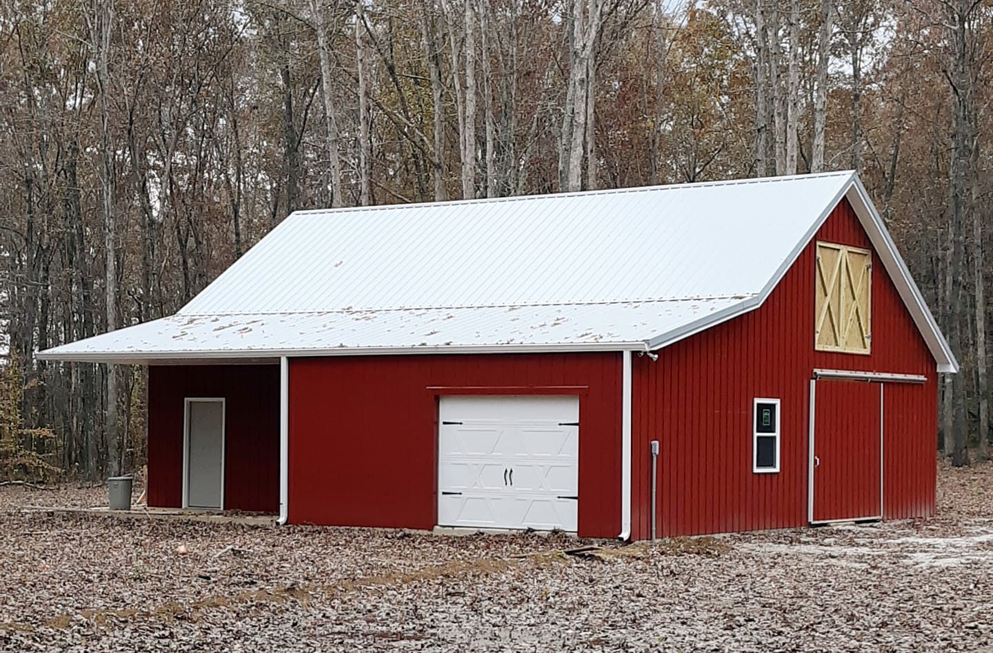 A red barn with a white roof is surrounded by trees.