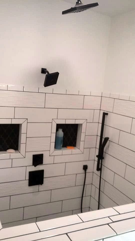 A shower with white tiles and a black shower head