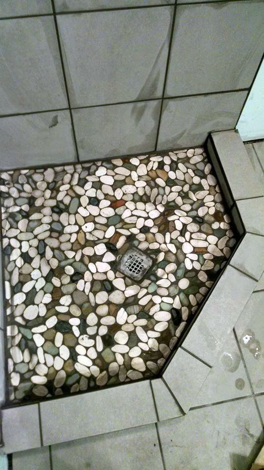 A shower stall with a stone floor and a drain