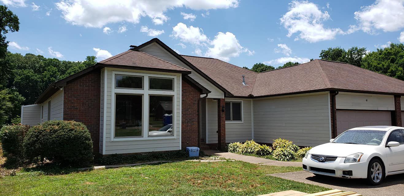 A white car is parked in front of a brick house.