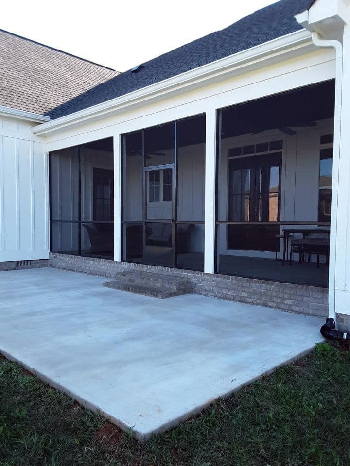 A screened in porch with a concrete patio in front of a house.