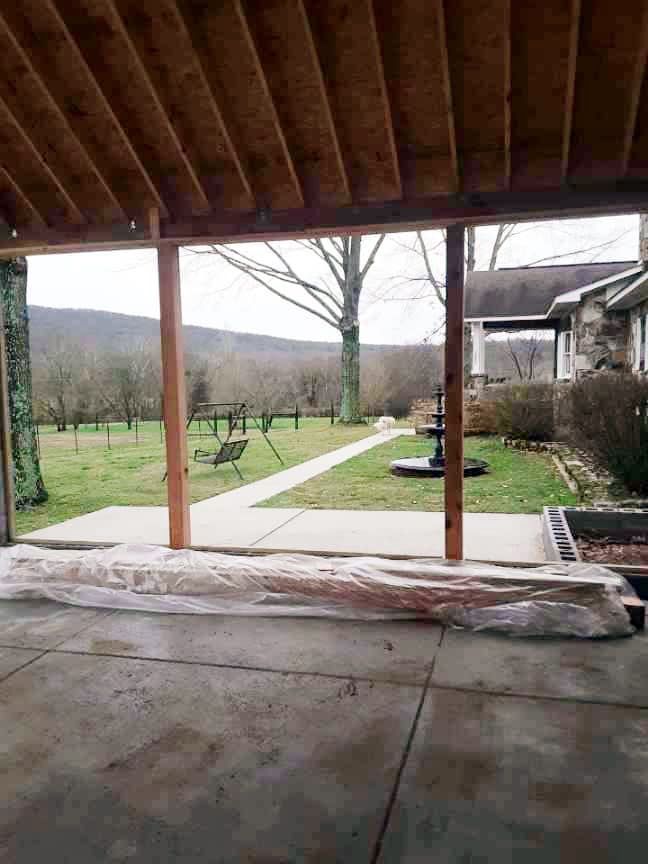 A covered patio with a view of a yard and a house in the background.