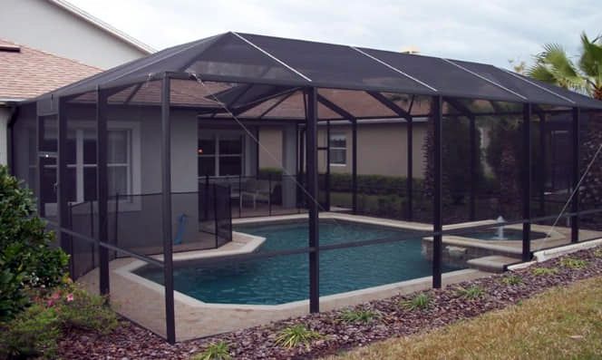 A screened in swimming pool with a house in the background