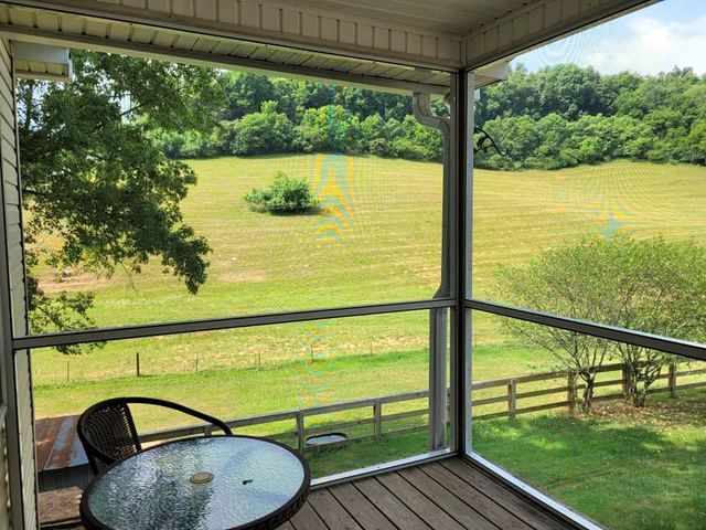 A screened in porch with a table and chairs and a view of a field.