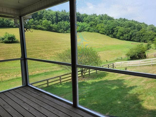 A screened in porch with a view of a field and a fence.