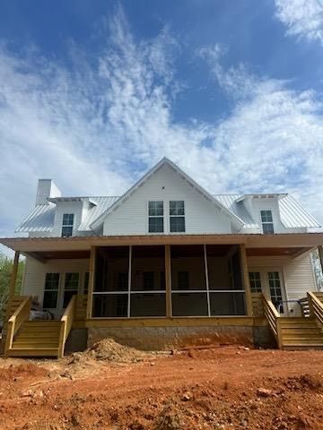 A large white house with a screened in porch is sitting on top of a dirt field.