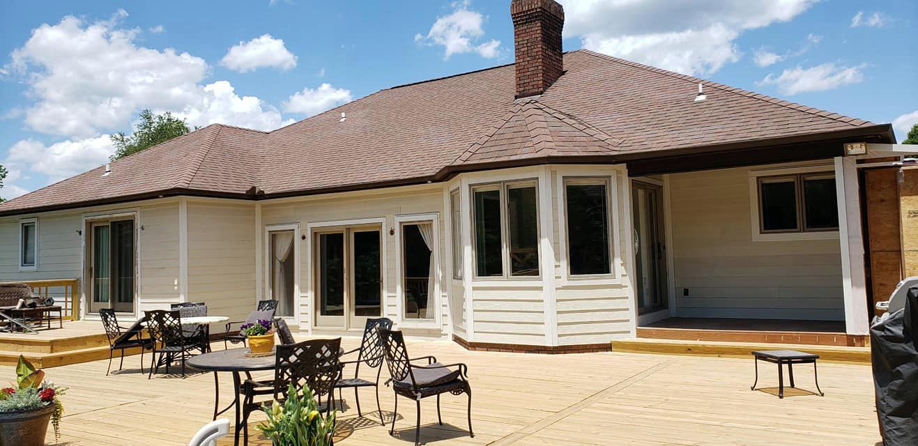 A large white house with a brown roof and a patio with tables and chairs.