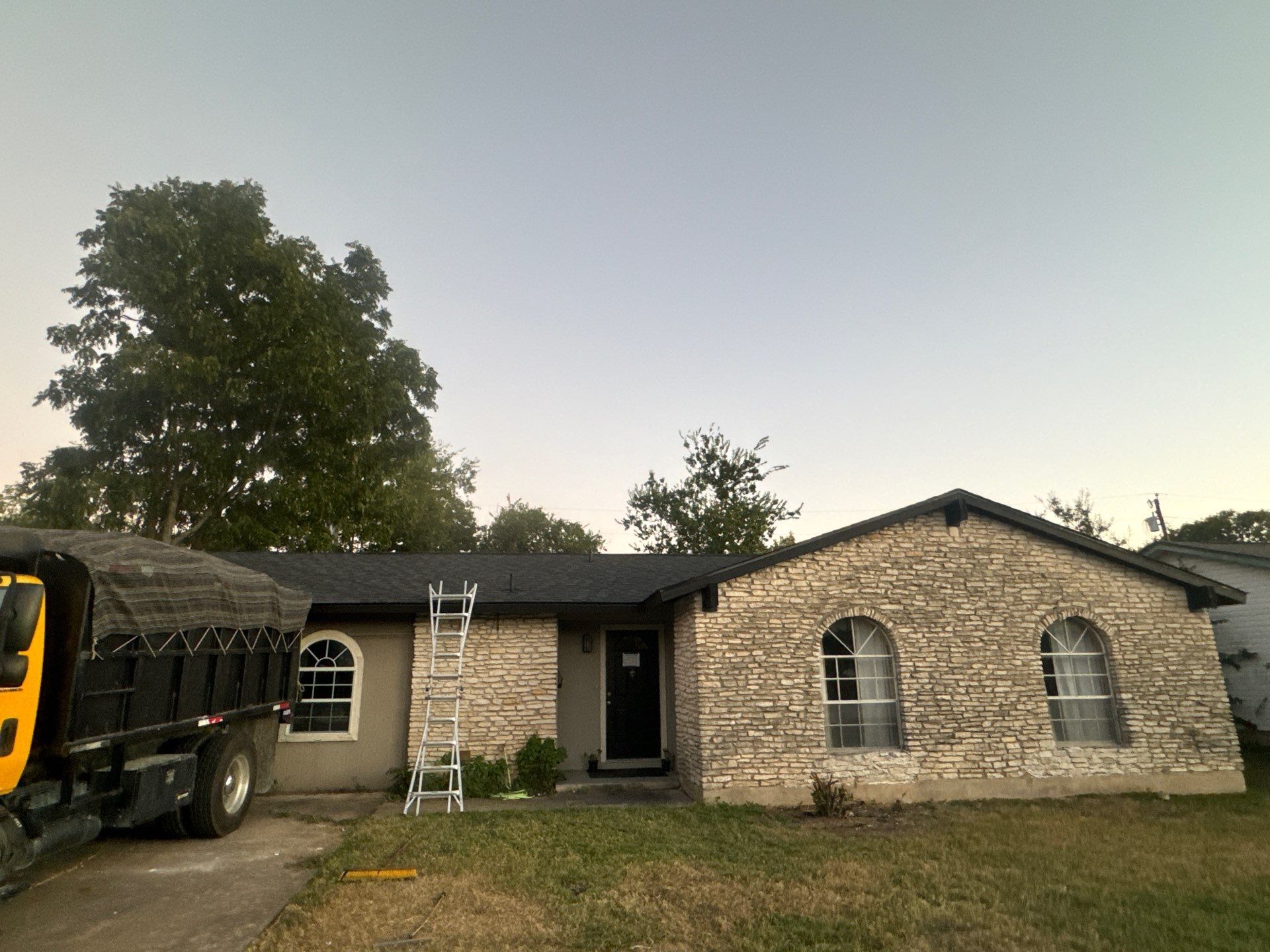 A truck is parked in front of a house with a ladder on the roof.