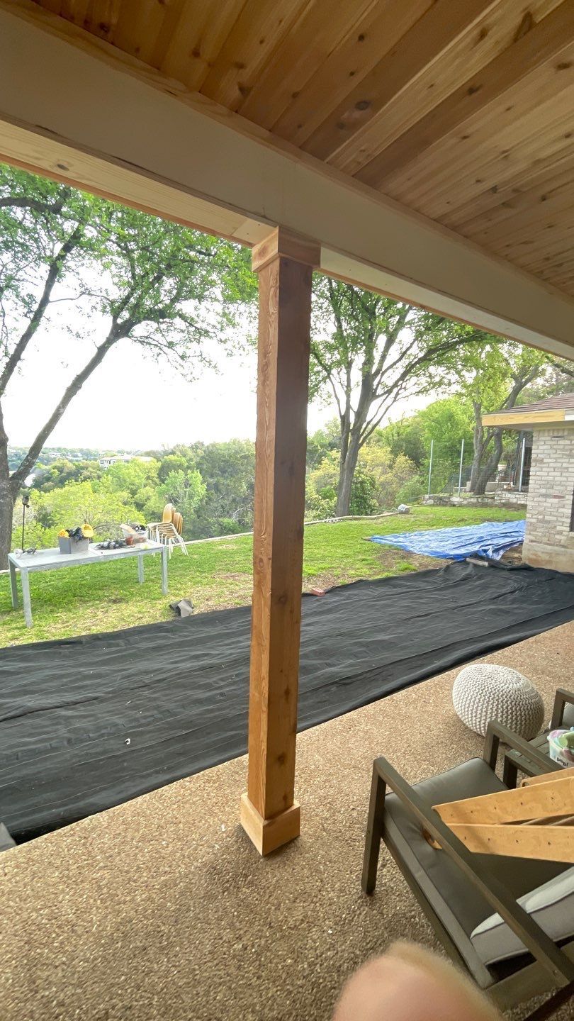 A person is standing under a covered patio with a view of a yard.