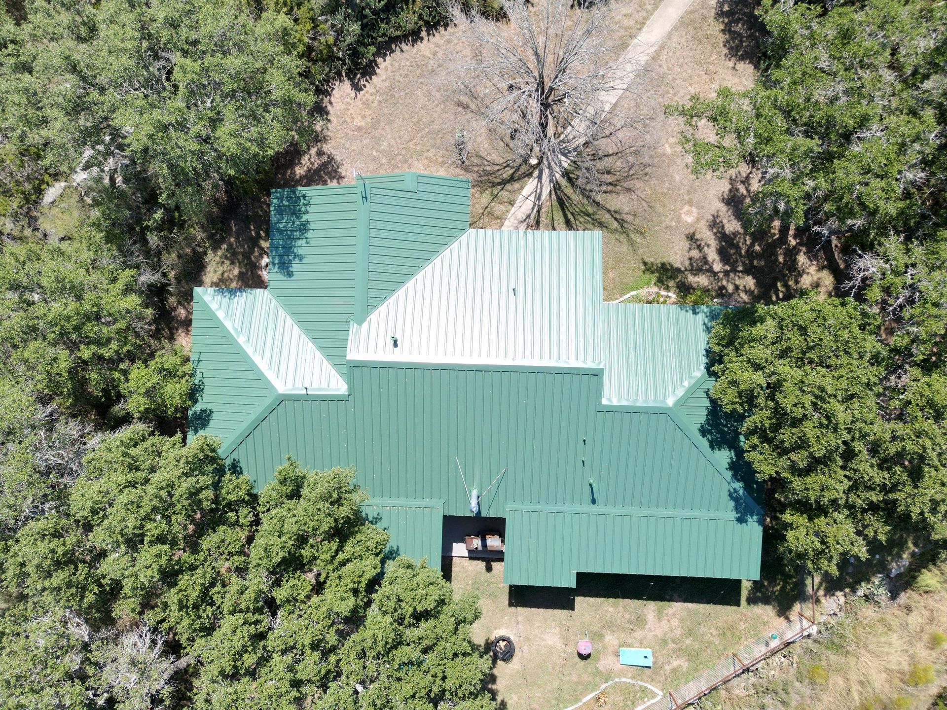An aerial view of a house with a green roof surrounded by trees.