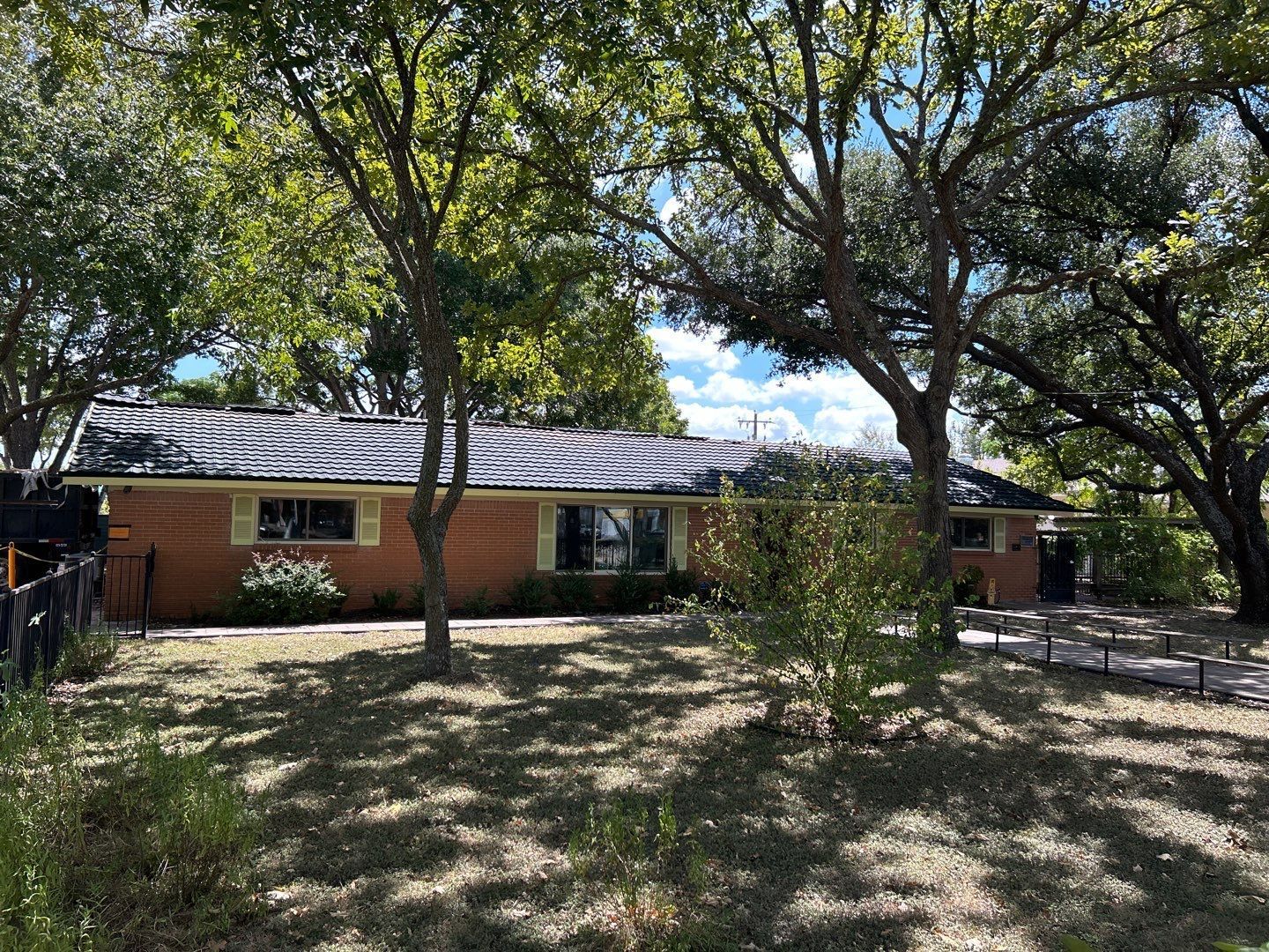 A brick house with a fence and trees in front of it.