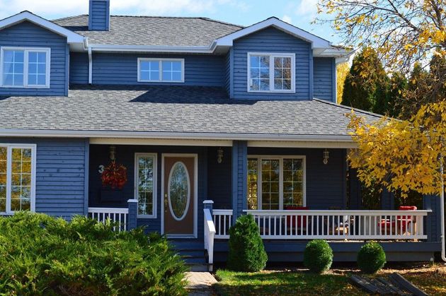 Blue two-story house with a porch, white trim, and autumn trees in front