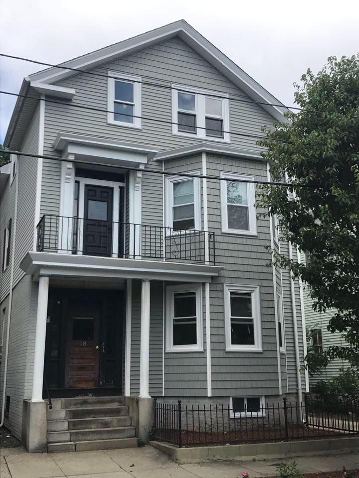 Gray three-story house with white trim, front porches, and a small fenced yard