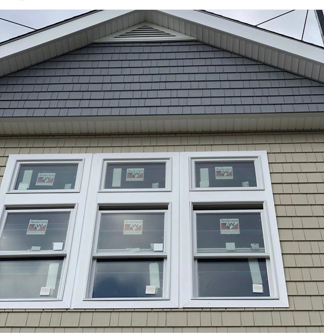 White-framed windows beneath a gray gabled roof on a light beige house exterior