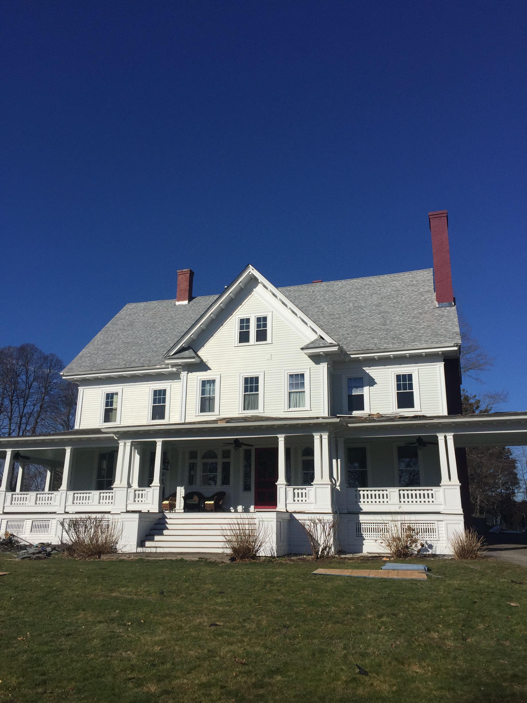White farmhouse with a porch and red chimneys under a clear blue sky