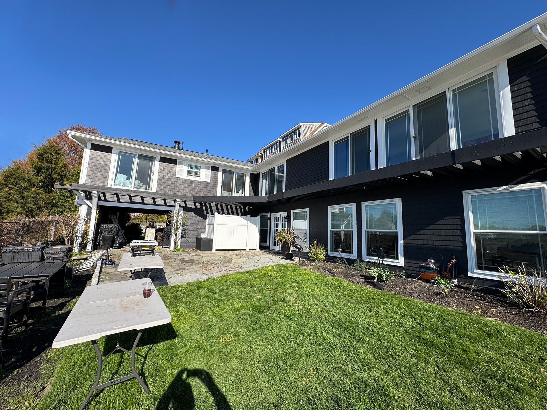 Sunny backyard with green lawn and a modern house with large windows and patio deck