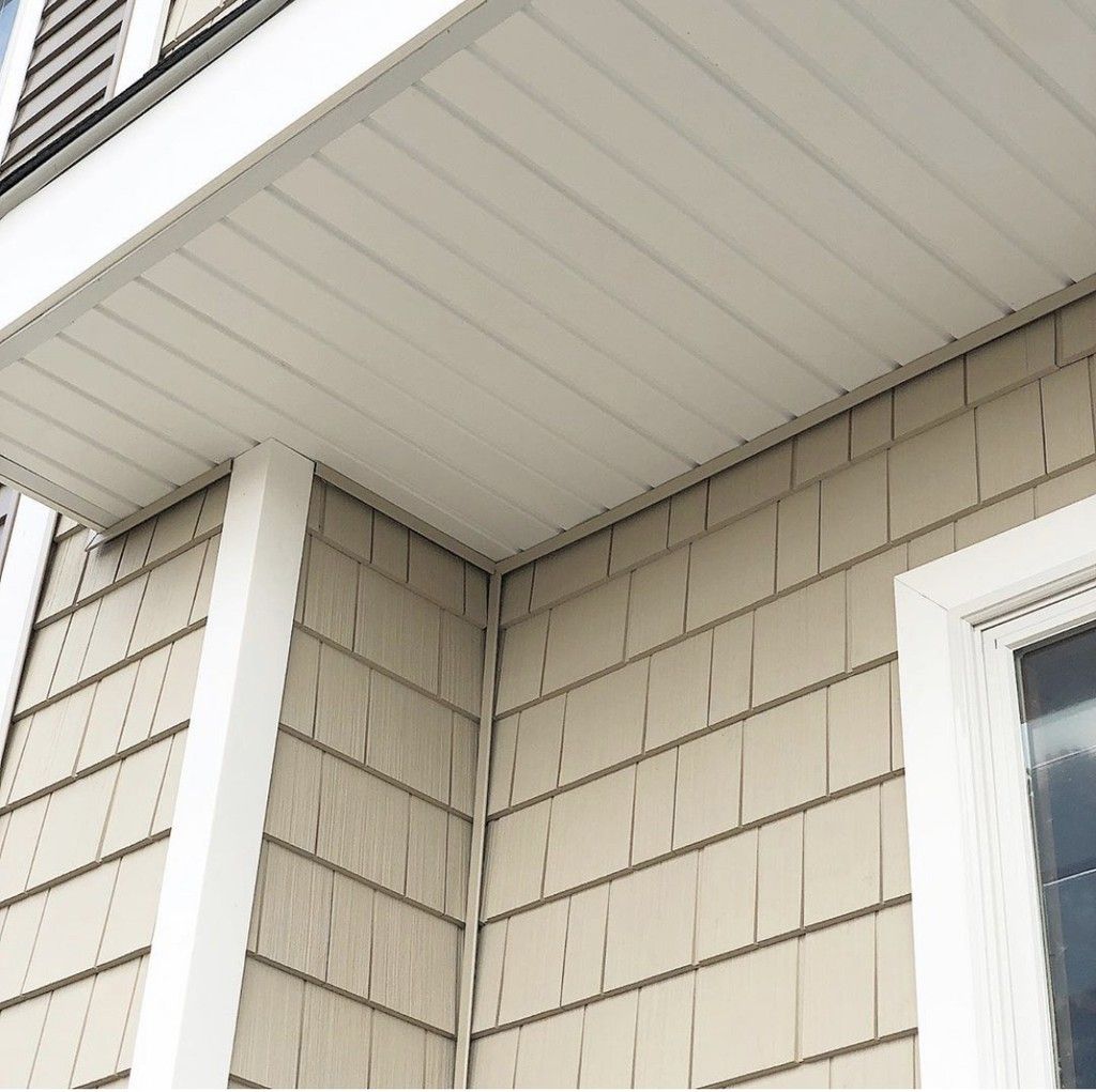 Close-up of beige house siding, white trim, and soffit under the roof eave