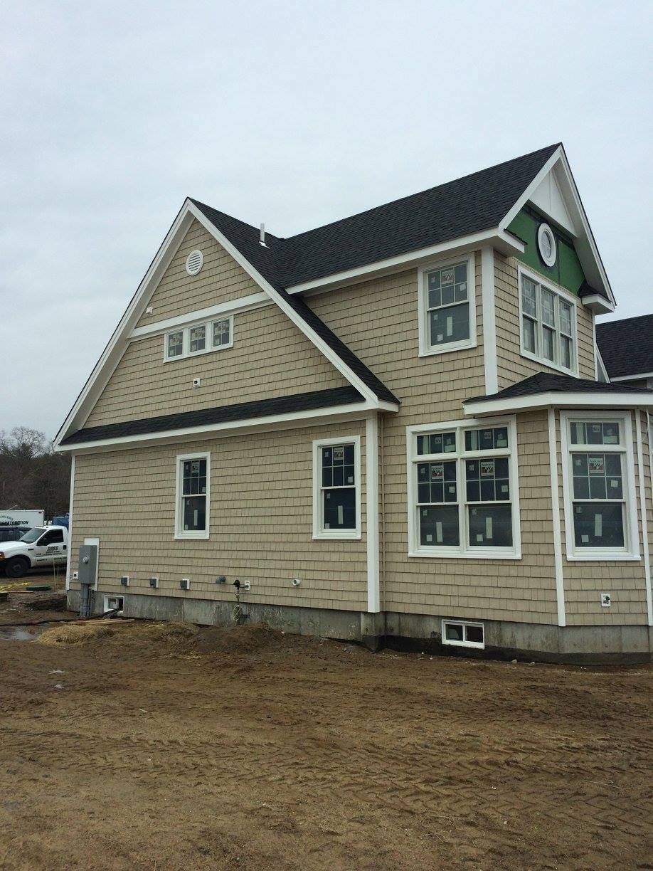 New beige house with green trim and dark roof on a muddy construction lot