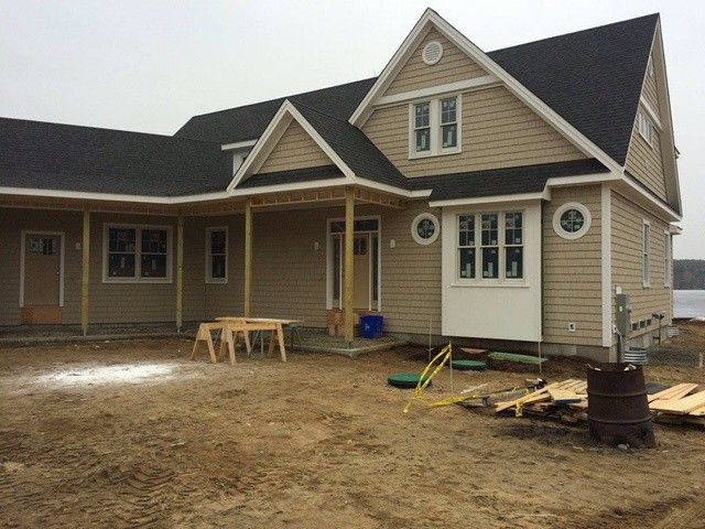New beige house with porch and garage under construction, with tools and dirt yard in front