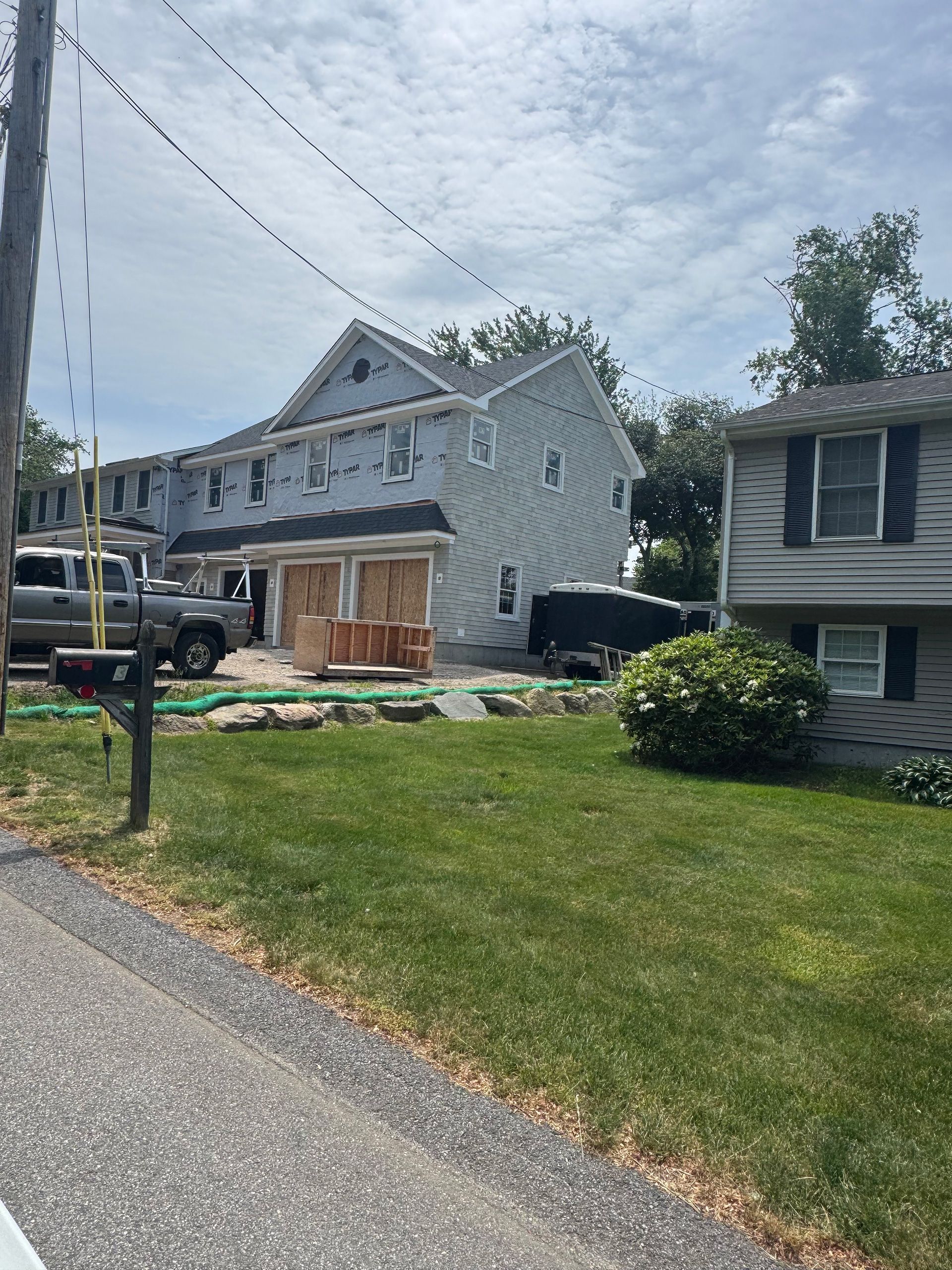 Grey stone house with a large front lawn, parked truck, and neighboring homes on a quiet street