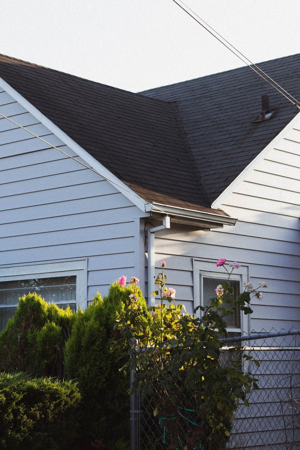 White house with dark roof, front shrubs, and a chain-link fence in the yard